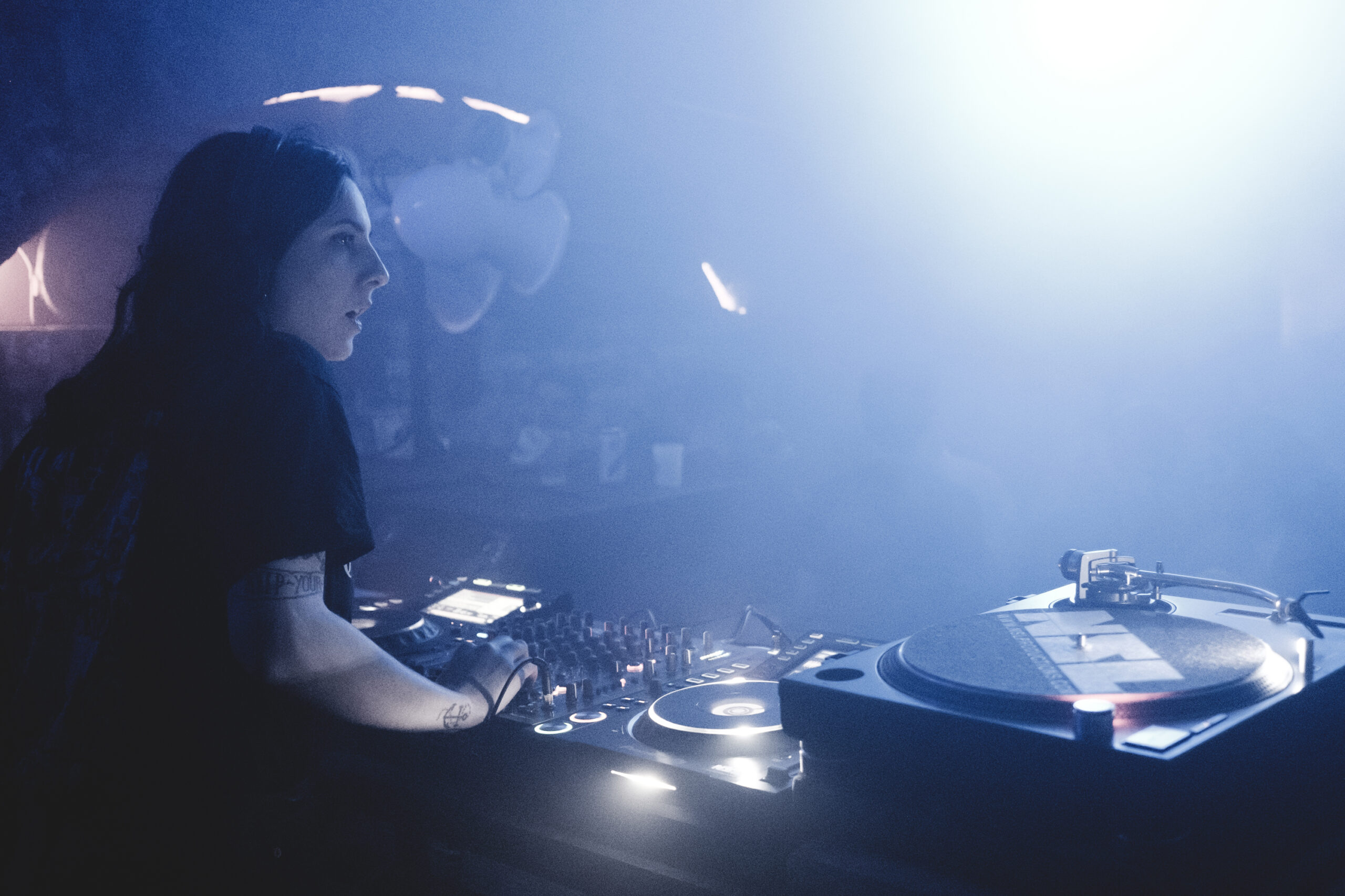 A woman with black hair DJ's in a smokey club.
