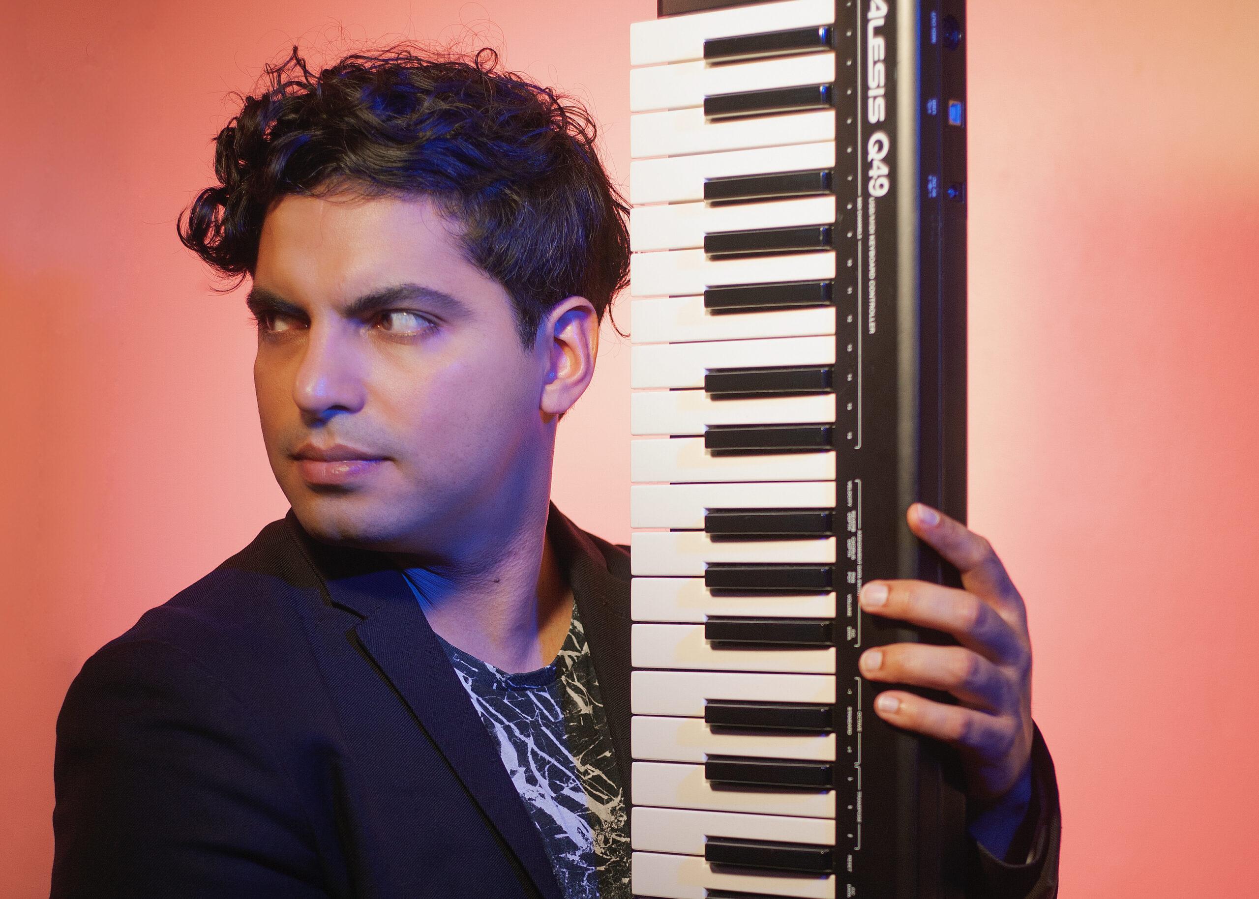 The artist Zubin Kanga holds a keyboard infront of a peach coloured background. 