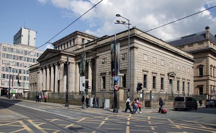 A white brick building set on a crossroad with Roman style pillars out front and an arched roof.