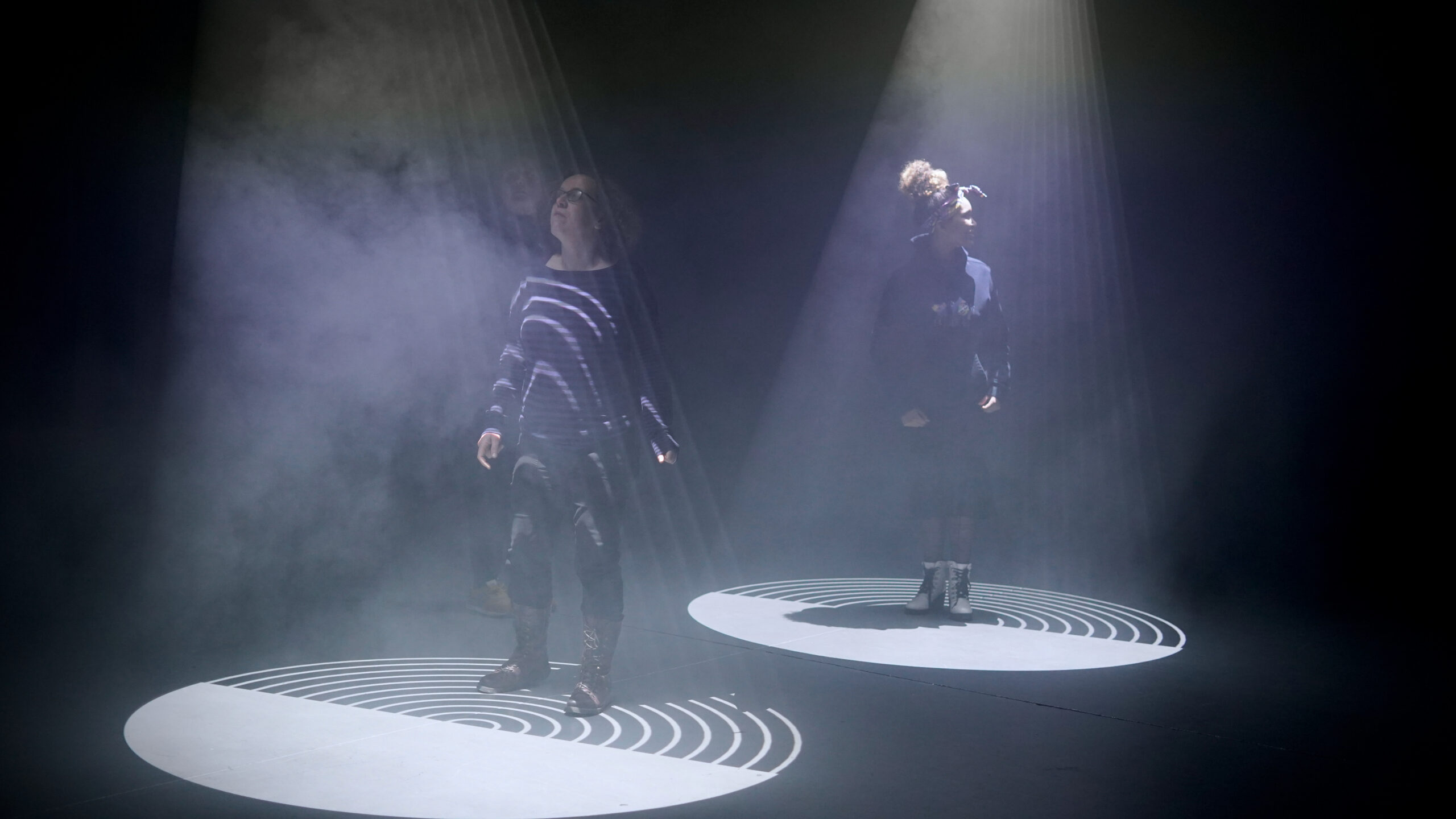 Two people stand in pools of projected light